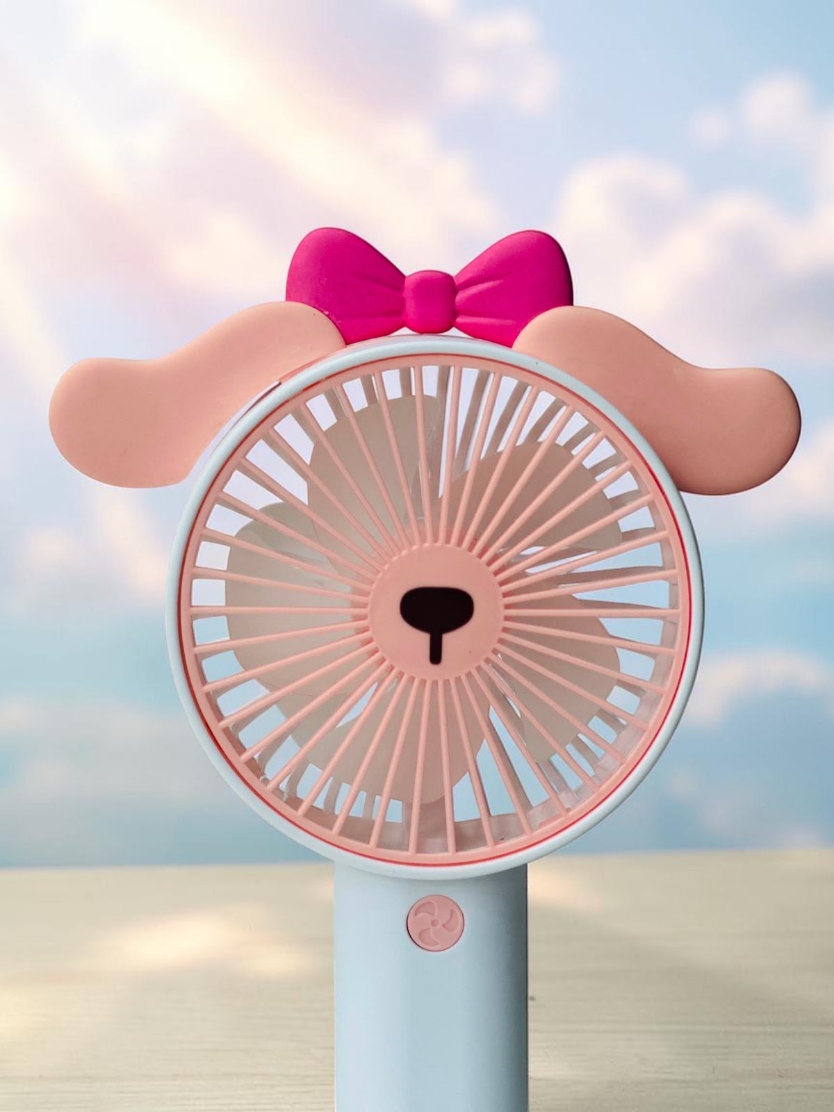 Miso station portable animal handheld fan in pastel pink with floppy ears and a bright pink bow against a sky background
