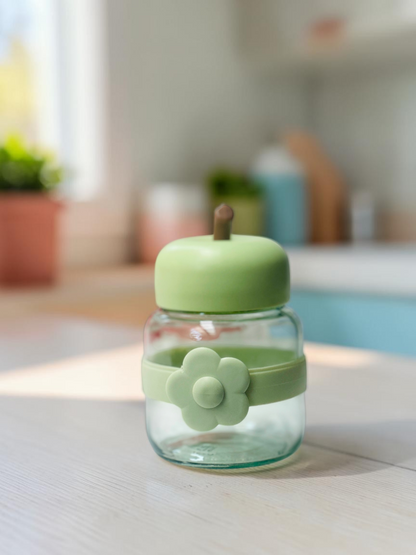 Miso station apple-shaped glass storage jars with colorful silicone lids and flower-accented bands on a white surface.