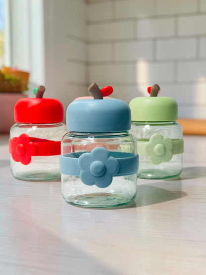 Miso station apple-shaped glass storage jars with colorful lids and flower-accented silicone bands on a white surface.