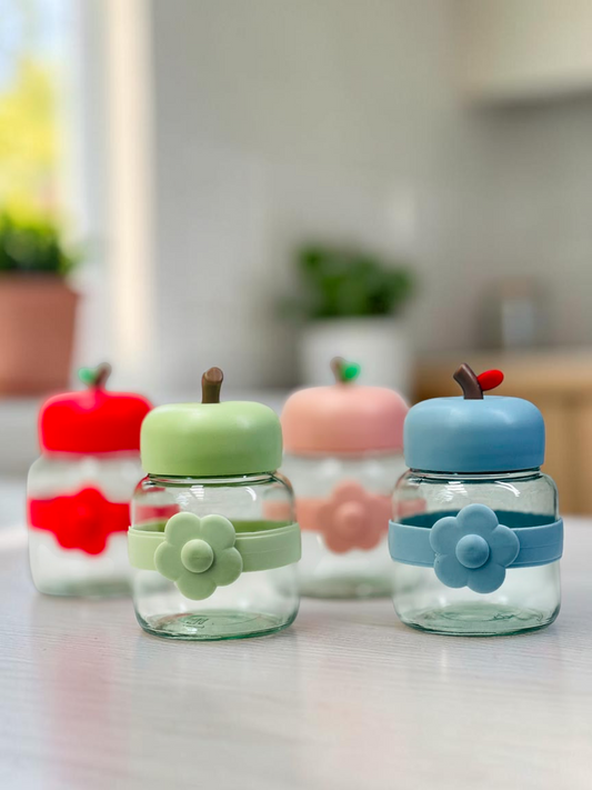 Miso station apple-shaped glass storage jars with colorful silicone lids and flower-accented bands on a kitchen table.