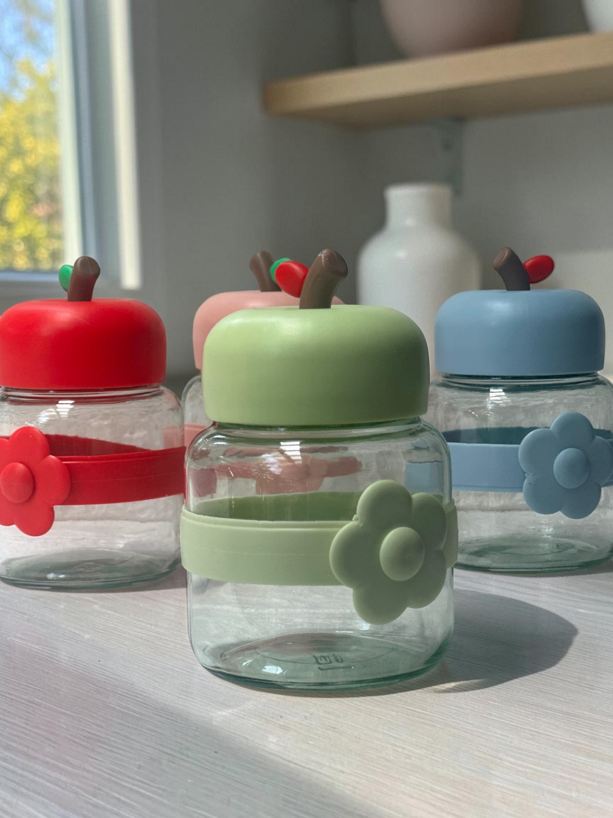 Miso station apple-shaped glass storage jars with colorful lids and flower-accented silicone bands on a white surface.