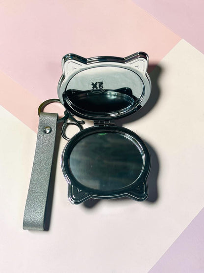 Miso station cat shaped silver metallic compact mirror with a keychain and wrist strap, open to show dual mirrors.