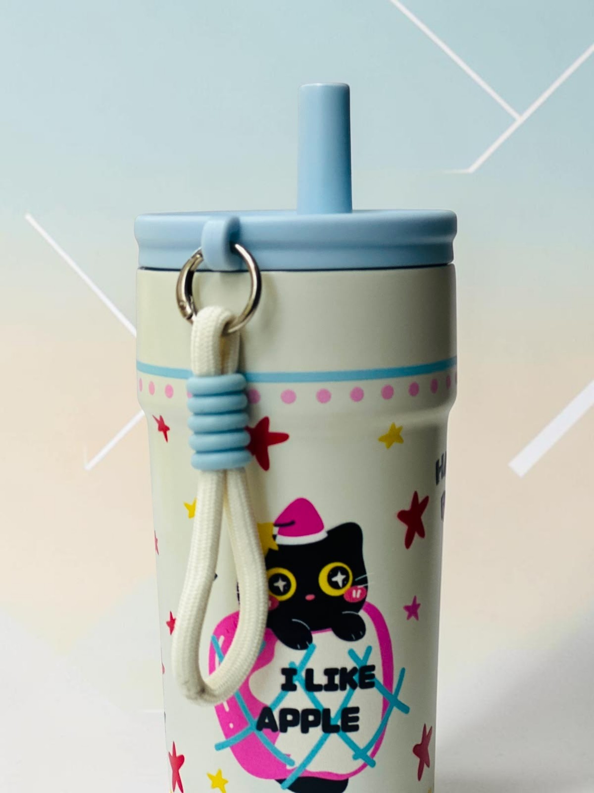 Miso station cream insulated tumbler with a black cat in apple graphic, blue lid, straw, and carrying strap.