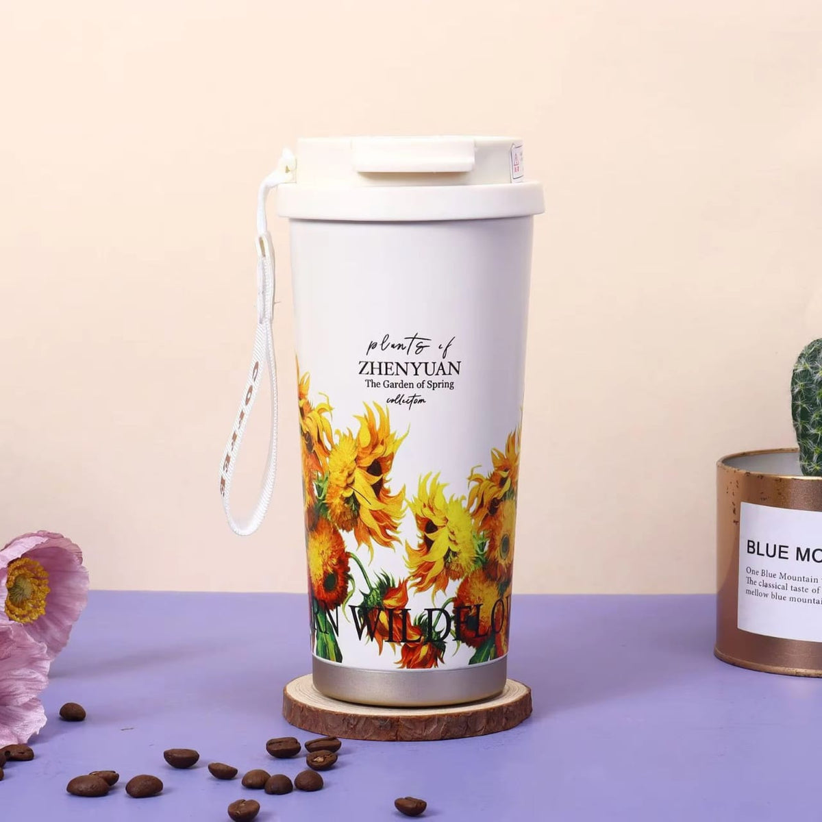 Miso station insulated travel tumbler with sunflower floral print, white lid, and carrying strap on a wooden coaster.