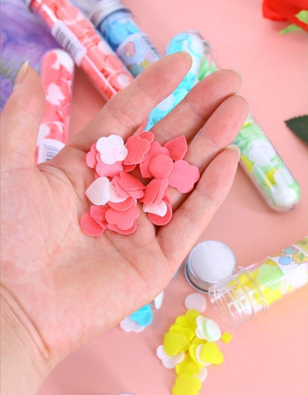 Miso station portable fruit scented flower shaped soap confetti flakes in a hand with travel tubes on a pink surface