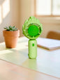 Miso station mint green lotus-inspired portable handheld rechargeable fan on a white faux fur background