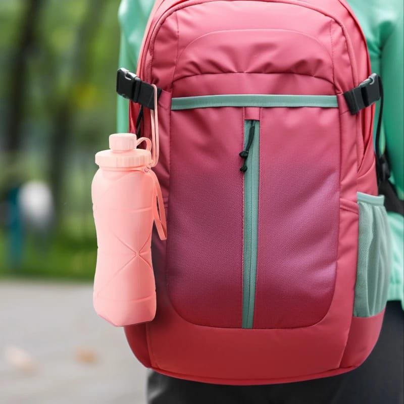 Miso station pink silicone collapsible water bottle clipped to a red hiking backpack for travel and outdoor activities