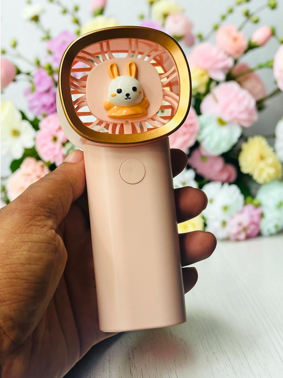 Miso station pastel pink handheld fan featuring a cute rabbit character and gold-tone rim held against floral decor.