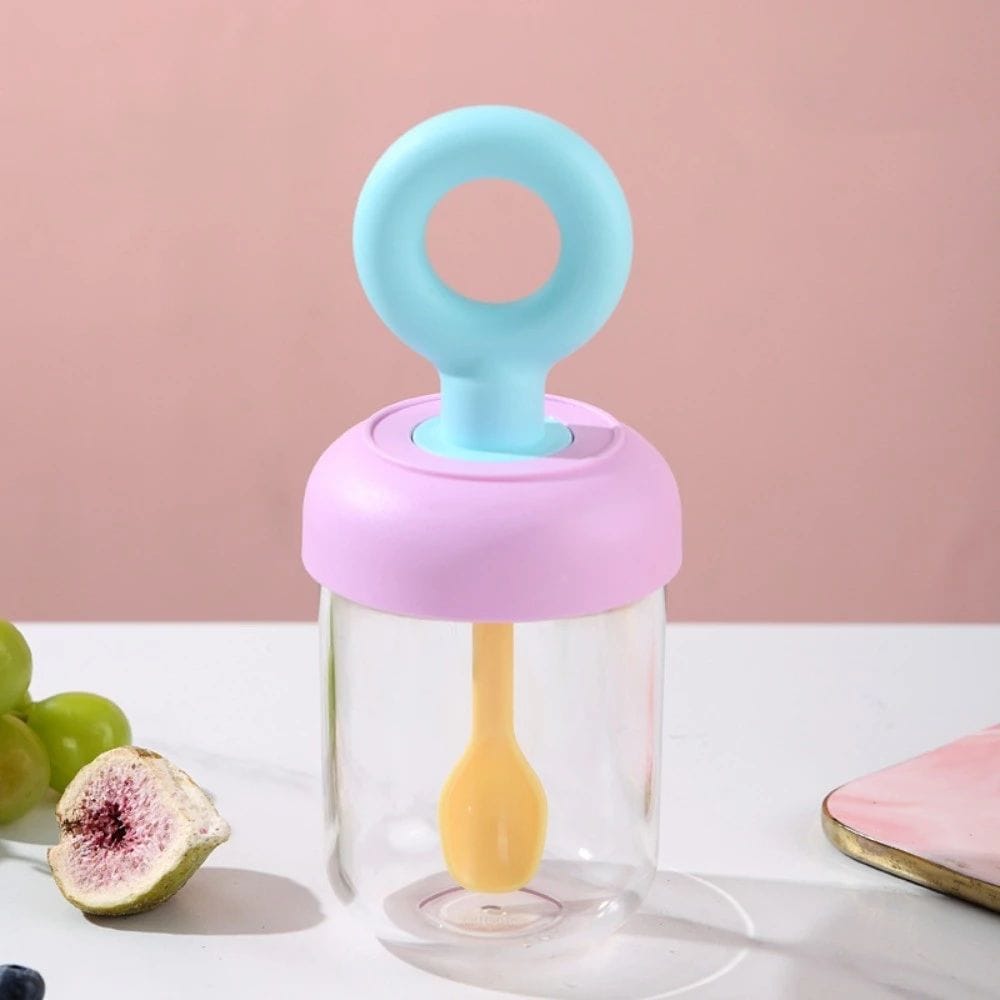 Miso station portable yogurt cup with a pink lid, blue handle, and integrated yellow spoon on a white surface.