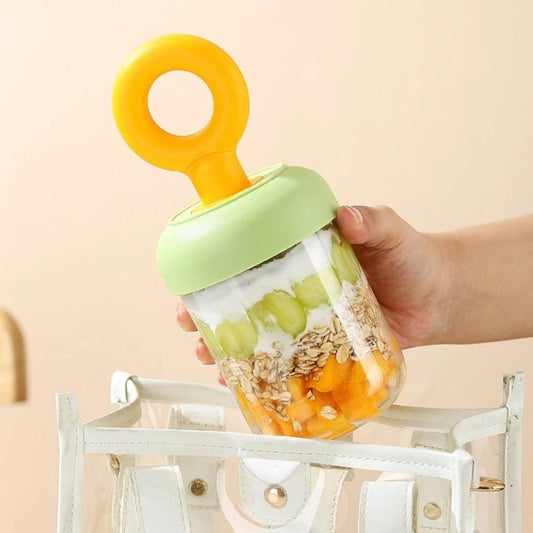 Miso station portable yogurt cup with green lid and yellow handle, filled with fruit and oats, held over a bag.