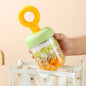 Miso station portable yogurt cup with green lid and yellow handle, filled with fruit and oats, held over a bag.