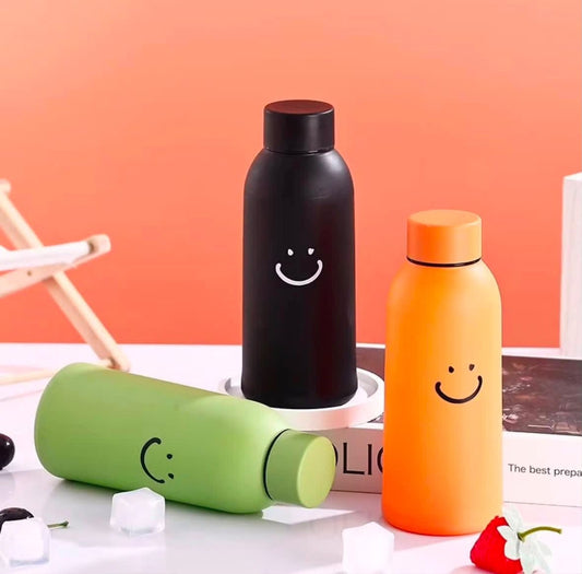 Miso station insulated water bottles in black, orange, and green with minimalist smiley face designs on a desk.