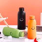 Miso station insulated water bottles in black, orange, and green with minimalist smiley face designs on a desk.