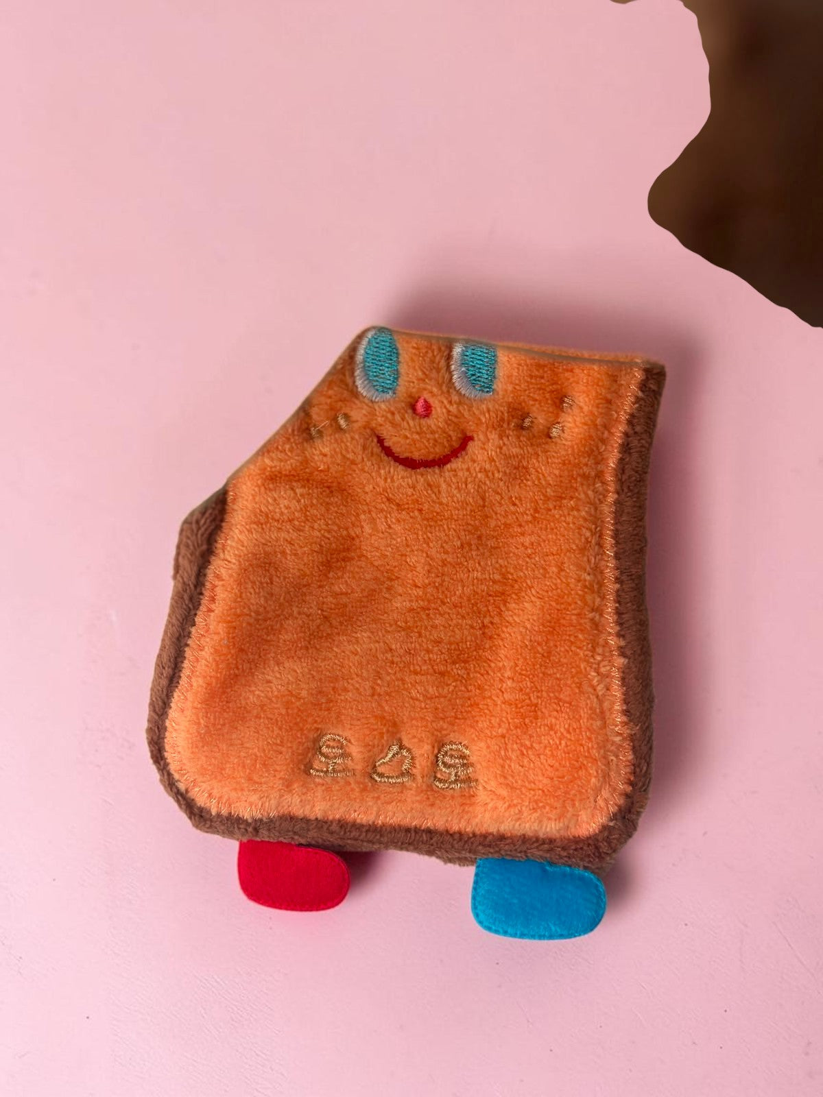Miso station toast-shaped cleaning sponge with a cute embroidered face, orange plush texture, and small colorful feet.