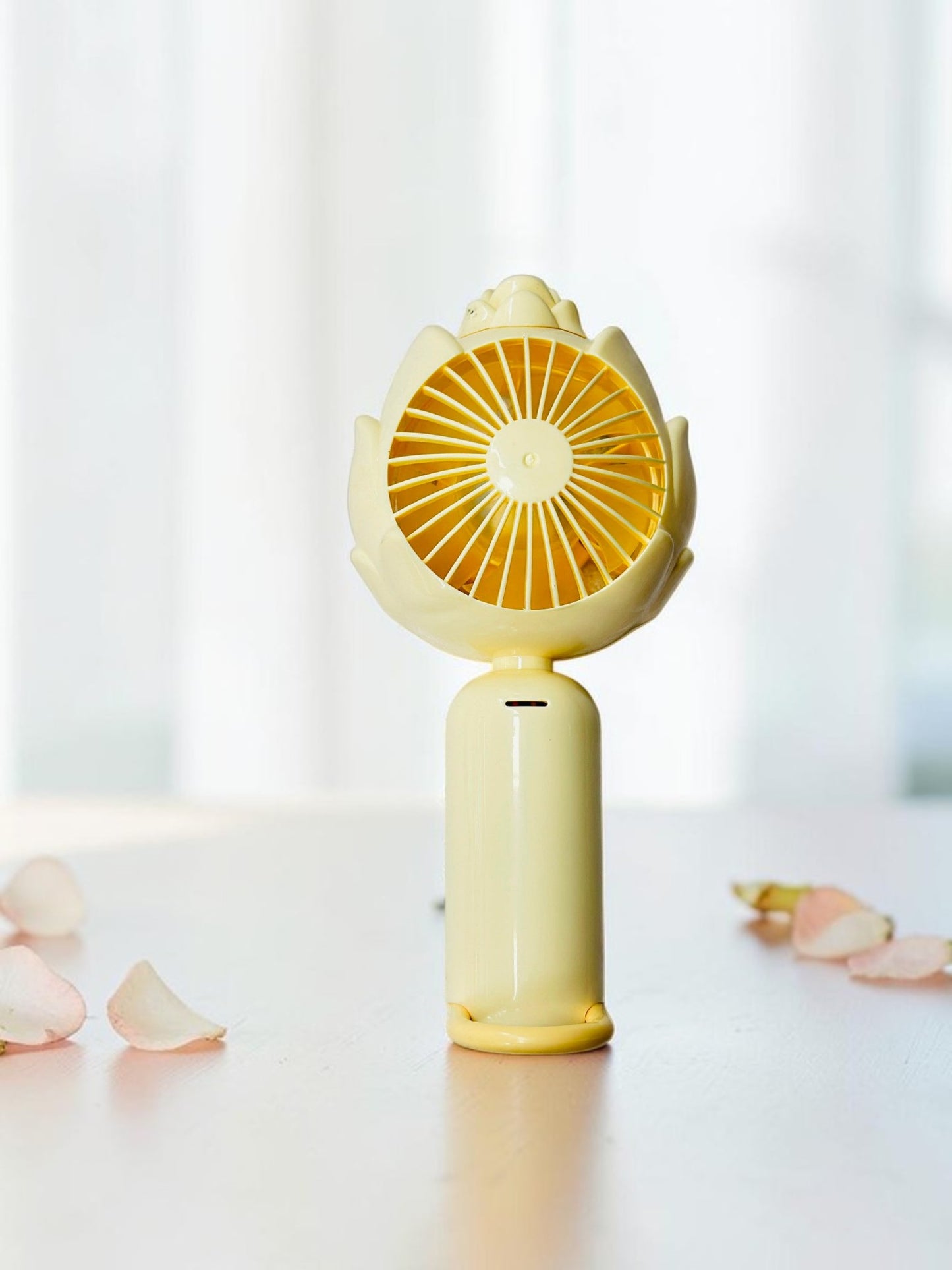 Miso station yellow lotus-inspired portable handheld rechargeable fan with petal-shaped housing on a table.